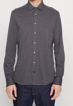 Chemise grise à manches longues avec col boutonné, boutons sur le devant, et petit logo sur la poitrine. Matière en coton, texture lisse.