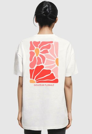 Weißes T-Shirt mit einem bunten Blumendesign auf der Rückseite in Rottönen, Rosa und Orange, mit dem Text "Douceur Florale" darunter.