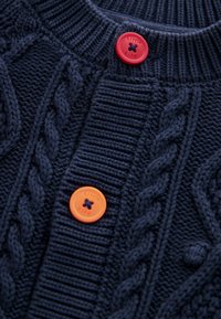 Marine gebreide trui met een textuurpatroon, voorzien van oranje en rode knopen met de tekst "Little Bird". Accent kabels voegen visuele interesse toe.