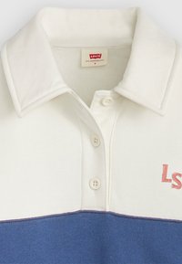 Polo shirt a strisce bianche e blu navy con texture morbida, colletto ripiegato e patta con tre bottoni. Presenta un dettaglio ricamato "LS" in rosa.