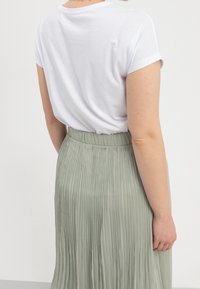 Bílý bavlněný tričko s ohrnutými rukávy, kombinované se světle zelenou plisovanou sukní s širokým pasem a vertikálními pruhy.