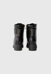 Bottines en cuir noir avec une finition lisse, présentant un bout arrondi, un petit talon carré et des accents de double zip doré à l'arrière.