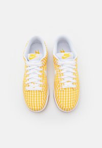 Scarpe da ginnastica Nike con motivo a quadretti gialli e bianchi, lacci bianchi e suole in gomma. Il design è basso con colletto imbottito.