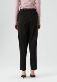 Pantalon noir sur mesure à coupe droite, doté d'une texture lisse et d'une poche arrière, porté avec un pull rose clair.