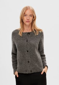Grå stickad cardigan med rund halsringning, fem svarta knappar fram och långa ärmar. Texturerad ull med en något lös passform.