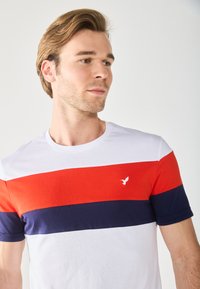 T-shirt pour homme avec des rayures horizontales blanches, rouges et bleu marine. Matière en coton doux, col rond et petit logo.