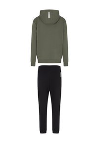 Felpa verde oliva con cappuccio foderato e strisce bianche sul retro; abbinata a pantaloni sportivi neri con logo laterale. Tessuto in misto cotone.