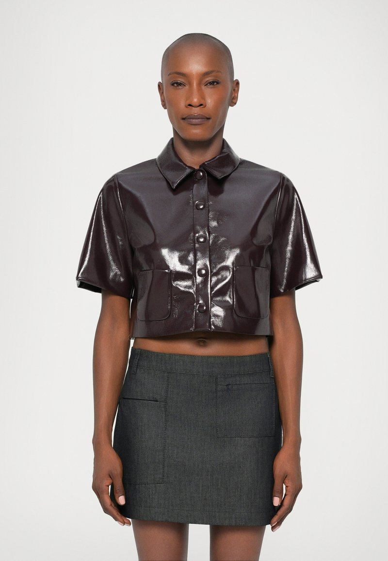 Bordó fényes, rövid ujjú cropped ing, elöl gombos záródással, sötét szürke mini szoknyával párosítva, amely elülső zsebekkel rendelkezik.