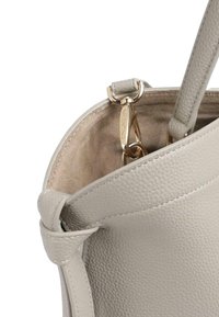 Primo piano di una borsa in pelle grigio chiaro con trama, che mostra l'interno in camoscio e la chiusura in metallo color oro incisa con Valentino.