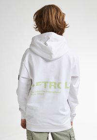 Felpa bianca con un grande logo verde sulla schiena. Presenta un cappuccio con cordino e una vestibilità comoda. Indossata con pantaloni cargo verde chiaro.