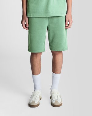 Person som har på seg grønne shorts, hvite ankelsokker og hvite joggesko, står mot en ensfarget lys bakgrunn.