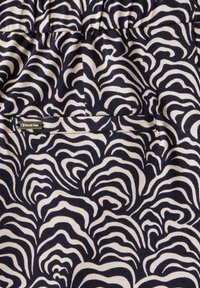 Bavlněná látka s námořnickým a krémovým vlnitým vzorem. Obsahuje malou kovovou štítku s logem. Hladký povrch a elastický pás.