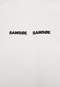 Sudadera blanca con dos frases bordadas "SAMSØE" en negro en negrita en el pecho, con una tela texturizada.