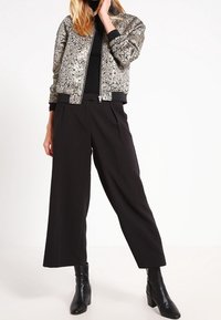 Kurtka typu bomber o metalicznym, teksturowanym wykończeniu, czarne ściągacze; zestawiona z czarnymi, szerokimi spodniami z wysokim stanem i botkami za kostkę.