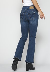 Mörkblå utsvängda jeans med medelhög midja, med en texturerad design på bakfickorna och en märkesskinnlabel vid midjebandet.