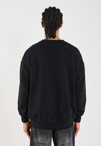 Black sweatshirt with dropped shoulders, ribbed neckline, and elasticated hem. Soft texture and relaxed fit. Worn with faded gray jeans.