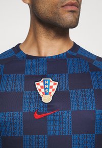 Marinblå atletisk tröja med blå textmönster "HRVATSKA". Har ett märke med röd och vit rutdesign och en Nike-logga i rött.