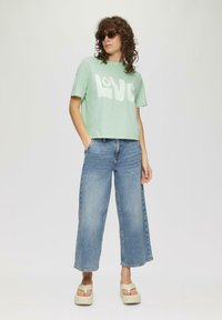 Miętowo-zielony krótki t-shirt z białym napisem "LOVE", w połączeniu z jasnoniebieskimi spodniami na szerokich nogawkach i beżowymi sandałami na platformie.