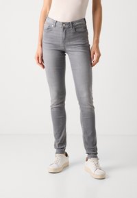 Smalbukser i lysegrå denim, høyt liv med fem lommer, subtil fading, og kombinert med hvite sneakers med synlige snørebånd.