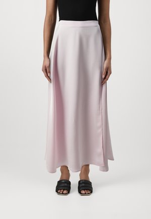 Jupe maxi fluide rose clair en tissu lisse, avec une taille ajustée et une fente latérale subtile, associée à des sandales noires à lanières.