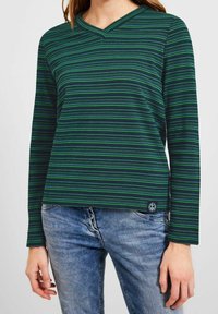 Grön och marinrandig långärmad topp med V-ringning, som har ett texturerat tyg och en liten logotyp patch vid fållen.