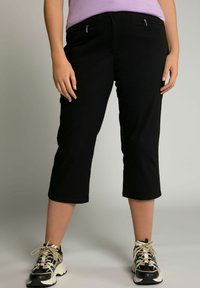 Zwarte cropped broek van zachte stof, met voorzakken met rits, een gladde textuur en een aansluitende tailleband. Gekleed met sportieve zwart-witte sneakers.
