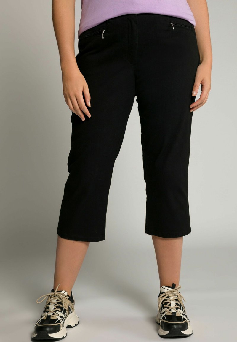Zwarte cropped broek van zachte stof, met voorzakken met rits, een gladde textuur en een aansluitende tailleband. Gekleed met sportieve zwart-witte sneakers.