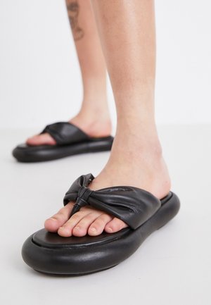 Las sandalias de piel negra cuentan con una correa ancha con un acento de nudo y una suela redondeada y acolchada. Acabado suave con una textura sutil.