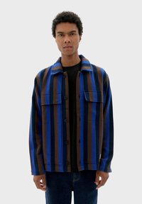 Gestreepte jas in blauw en bruin, gemaakt van dikke stof, met een knoopsluiting aan de voorkant, twee borstzakken en een kraag.
