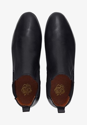 Paire de chaussures en cuir noir sans lacets avec bouts lisses et arrondis, semelles intérieures marron et petites languettes arrière, vues de dessus.