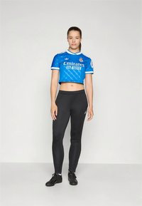 Blå kort topp med hvite detaljer, med teksten "Emirates Fly Better", kombinert med svarte leggings og svarte treningssko.
