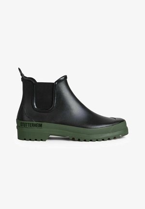 Zwarte rubberen Chelsea-boot met groene zool, gestructureerde afwerking, elastische zijpanelen en een treklus aan de achterkant. Kenmerkt zich door logo-detail aan de zijkant.