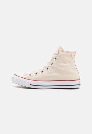 Beige højtop lærredsneakers med hvid gummisål, røde og sorte striber og hvide snørebånd mod en ensfarvet grå baggrund.