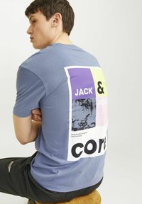 Blå bomulls t-shirt med en stor, flerfärgad grafik på baksidan med texten "JACK & JONES" och "core." Enkel rundhalsad design.