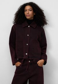 Burgundy denimjacka med spetsig krage, framknäppning med knappar, två fickor och dragsko i midjan. Strukturväv med en lätt lyster.