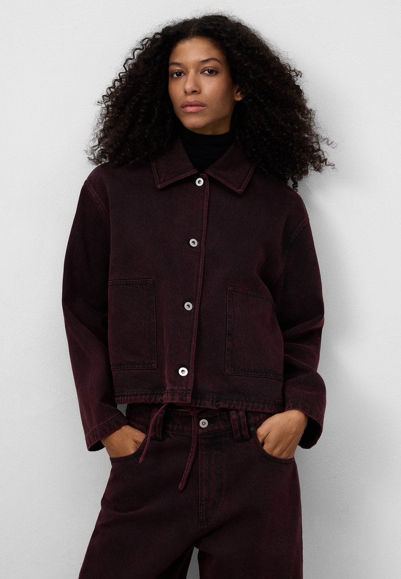 Burgundy denimjacka med spetsig krage, framknäppning med knappar, två fickor och dragsko i midjan. Strukturväv med en lätt lyster.