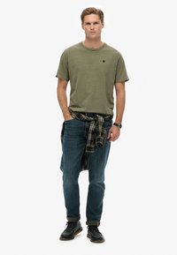 Oliwkowa bawełniana koszulka, niebieskie dżinsy, czarne skórzane buty i wiązana w pasie koszula w kratę. Prosty fason, luźny krój.