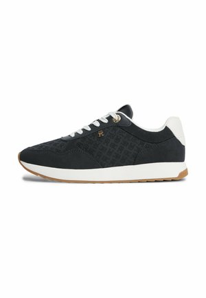 Zwart-witte lage sneaker met witte veters, een patroon aan de zijkant, een gouden logo-embleem, een witte hielstrook en een bruine rubberen zool.