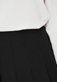 Pantaloni neri plissettati realizzati in un tessuto morbido, mostrati insieme a una maglietta bianca con vestibilità rilassata. Presentano linee pulite e un design minimale.