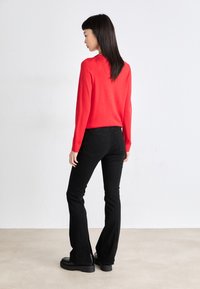 Top rojo de manga larga combinado con jeans negros de campana, con una cintura ajustada y pierna recta, complementado con zapatos negros robustos.