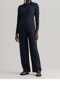Sweat-shirt en coton bleu marine à manches longues, avec poignets et ourlet côtelés ; associé à un pantalon bleu marine ample et des sandales plates.