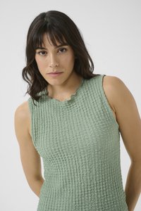 Haut sans manches vert clair avec un tissu texturé et froissé et un col en forme de scallop. Design simple, coupe ajustée et aspect doux.