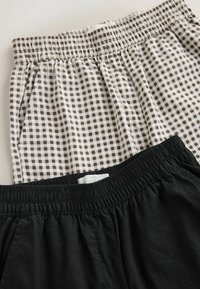Deux paires de shorts à taille élastique, l'une en lin noir et l'autre avec un motif à carreaux vichy noir et blanc.
