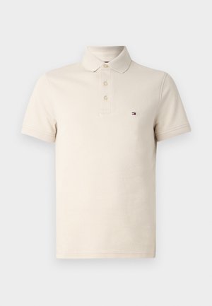Polo beige en coton avec un col classique, trois boutons et un petit logo sur la poitrine gauche. Manches courtes, tissu texturé.
