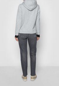 Sudadera gris con capucha ajustable, acentos en las muñecas en negro, combinada con jeans gris oscuro y calzado beige. Diseño simple, ajuste casual.