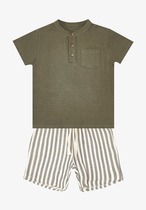 Camicia verde oliva a maniche corte con tre bottoni in legno e tasca sul petto abbinata a pantaloncini bianchi e grigi a righe verticali con coulisse.