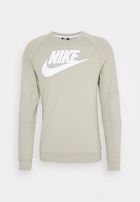 Sudadera Nike de cuello redondo en color beige claro, con mangas largas y un gran logotipo blanco de Nike y el swoosh centrado en el pecho.
