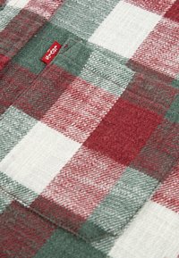 Rood en groen geblokt stof met witte accenten, met een zachte textuur. Een klein rood label is zichtbaar aan de rand van de stof.