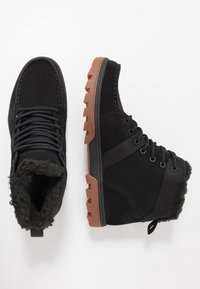 Czarne botki z teksturowaną cholewką, wyściełanym kołnierzem i gumową podeszwą. Posiadają sznurowanie oraz pętelkę ułatwiającą zakładanie.