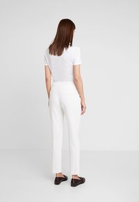Witte op maat gemaakte broek met een slim fit, voorzien van een middelhoge taille, achterzakken en een zachte textuur, gedragen met een eenvoudig shirt met korte mouwen.